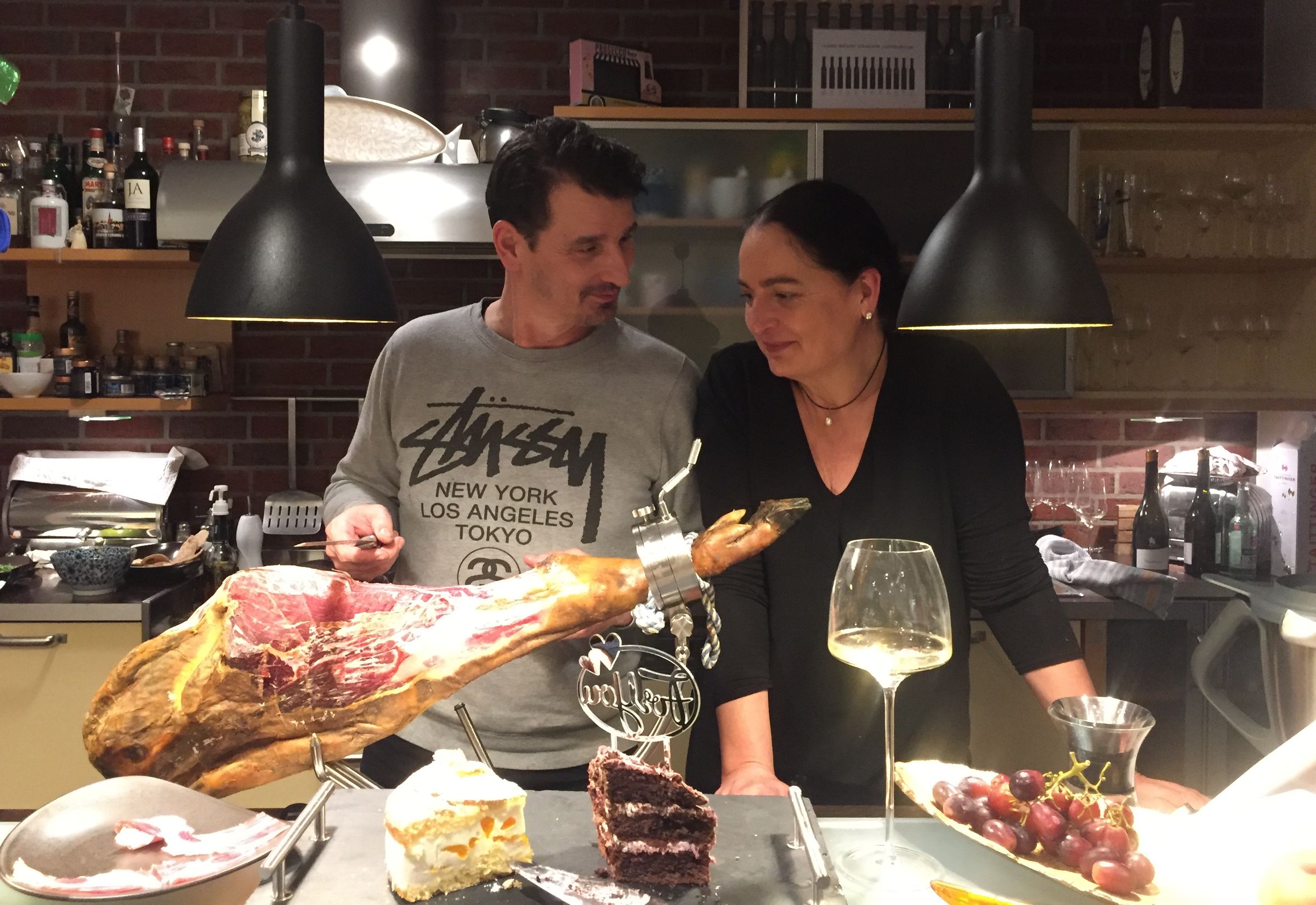 Marcel corta jamón a cuchillo mientras una invitada mira de cerca