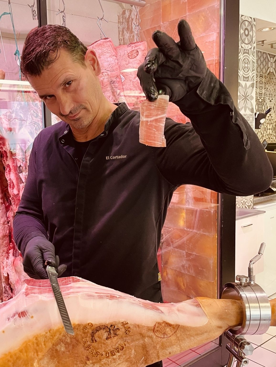 Marcel con guantes negros y cuchillo jamonero, mostrando una loncha recién cortada